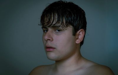 Close-up portrait of shirtless man against gray background