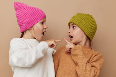 Sibling wearing knit hat gesturing against beige background