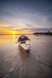 Boat moored on beach against sky during sunset