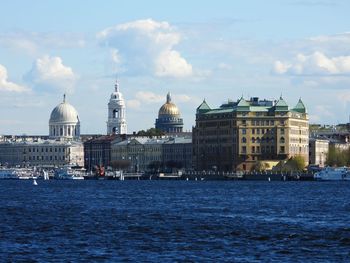 Buildings by river against cloudy sky