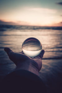 Person holding sunglasses against sea during sunset