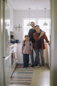 Portrait of smiling gay couple standing with daughter in kitchen at home