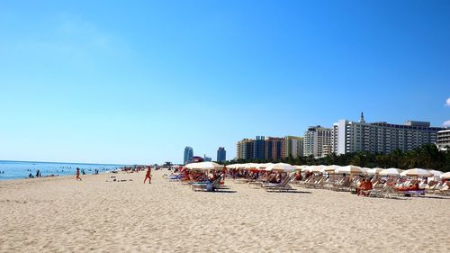 People on beach against clear blue sky