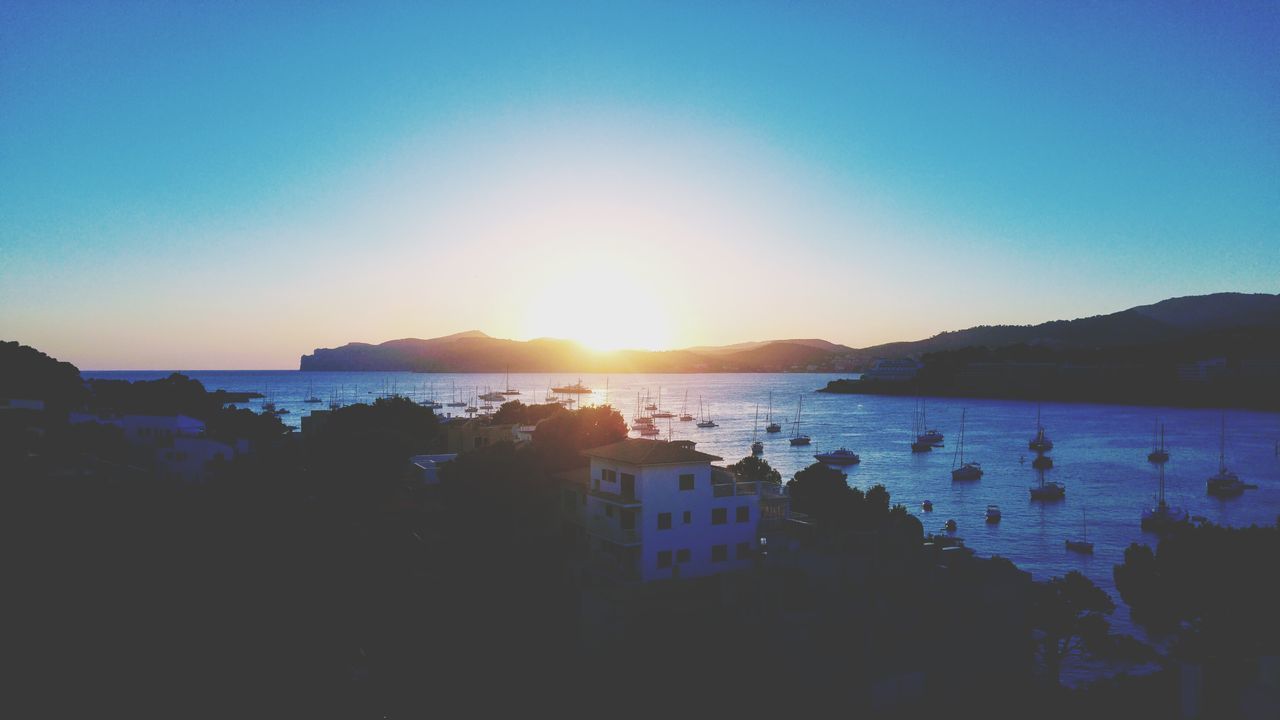 SILHOUETTE CITY BY SEA AGAINST SKY DURING SUNSET