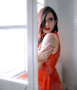 Portrait of young woman standing against window