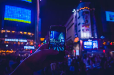 Cropped hand photographing illuminated buildings at night