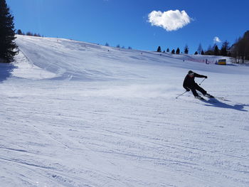 Man skiing on snow covered field against sky