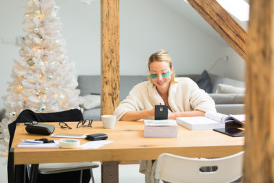 Smiling woman using mobile sitting at home