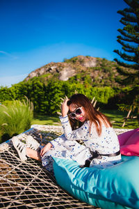 Woman sitting on mountain against blue sky