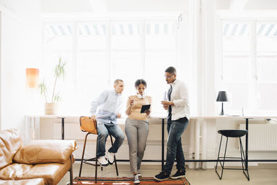 Full length of computer programmers looking at digital tablet while discussing by window in office