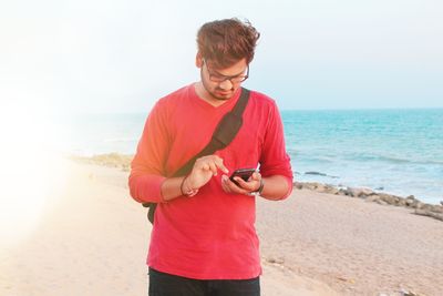 Young man using mobile phone at beach against sky