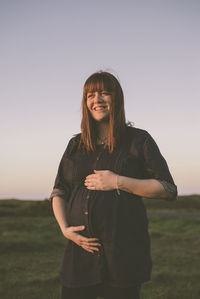 Happy pregnant woman standing on field against clear sky