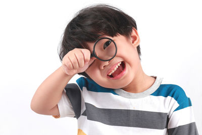 Portrait of smiling boy looking through magnifying glass against white background