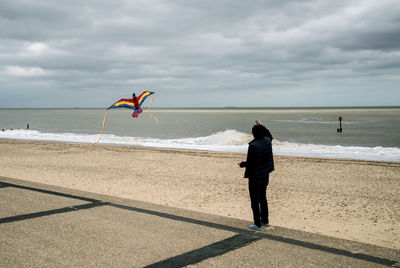 Full length of man flying kite by beach against sky