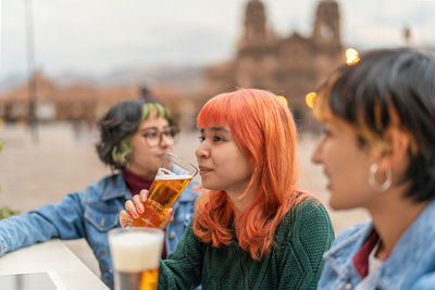 Side view of positive young female friends drinking beer while resting in outdoor pub in city of cusco