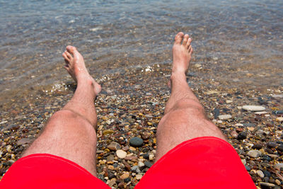 Low section of man relaxing on shore at beach
