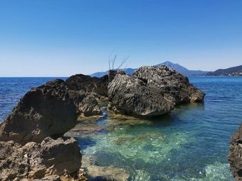 Rocks in sea against clear blue sky