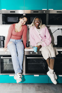 Portrait of cheerful young women sitting on kitchen counter in college dorm