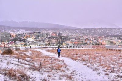 Rear view of man walking on snow against buildings in city