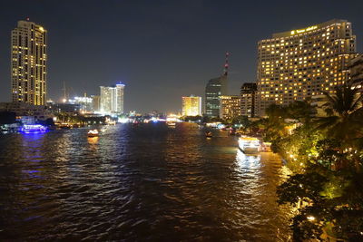 Illuminated buildings by river against sky at night