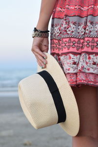 Midsection of woman with hat standing at beach