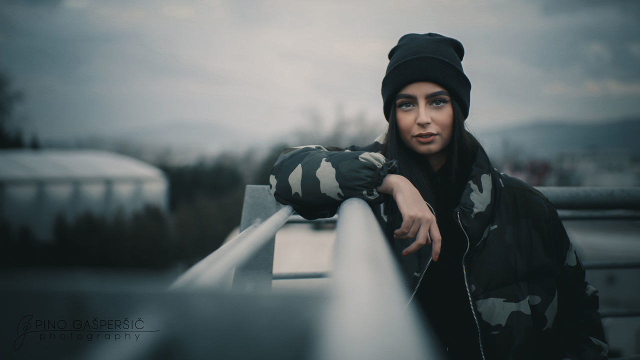 PORTRAIT OF BEAUTIFUL WOMAN HOLDING CAMERA AGAINST SKY