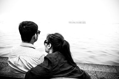 Rear view of couple sitting by sea against clear sky