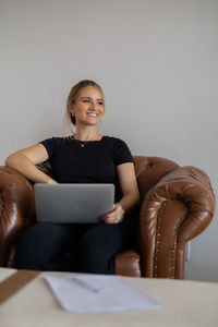 Woman working at home with laptop on a brown arm chair. home office concept. gray notebook.