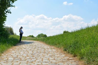 Rear view of a pregnat woman standing on footpath against sky