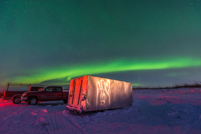 Illuminated car on snow covered field against sky at night