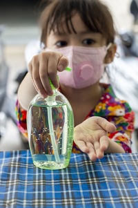 Cute girl wearing mask using hand sanitizer outdoors