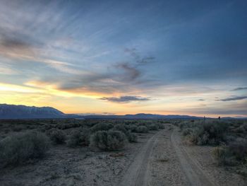 Dirt road amidst landscape against sky during sunset