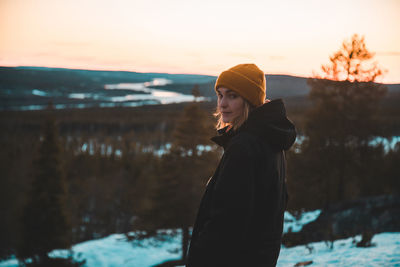 Side view of young woman standing against sea during sunset