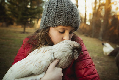 Girl kissing chicken while standing at poultry farm
