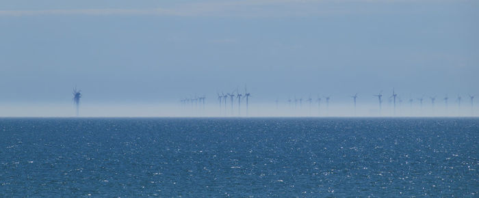 Scenic view of wind turbines against sky at sea