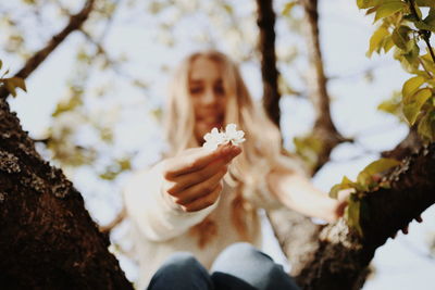 Midsection of woman holding flowering plant against trees