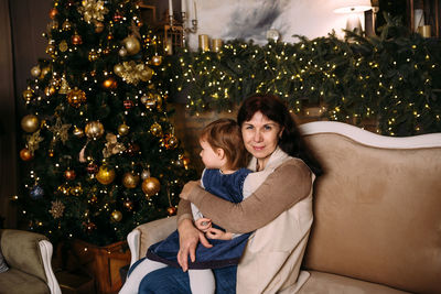 Portrait of smiling young woman sitting on christmas tree