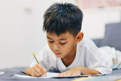 Cute boy writing in book at home