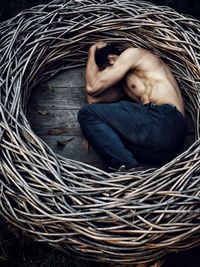 High angle view of muscular shirtless man lying in basket