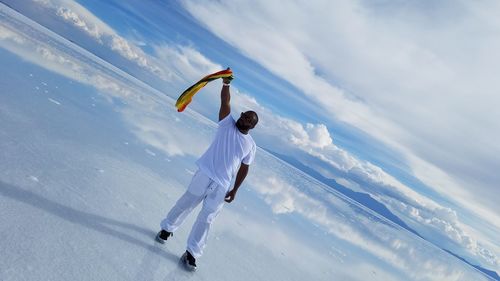 Full length of mature man holding scarf while standing on field against cloudy sky