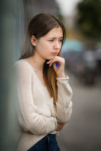 Thoughtful teenage girl looking away while standing in city