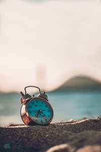 Close-up of clock on rock at beach against sky