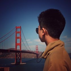 Side view of teenage boy looking at golden gate bridge against sky