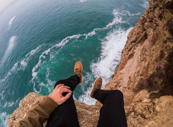 Low section of men sitting on cliff over beach