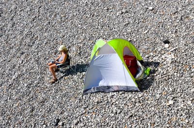 High angle view of person sitting in front of tent on stoney beach