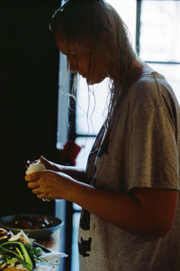 Side view of woman cutting vegetable while standing in kitchen at home