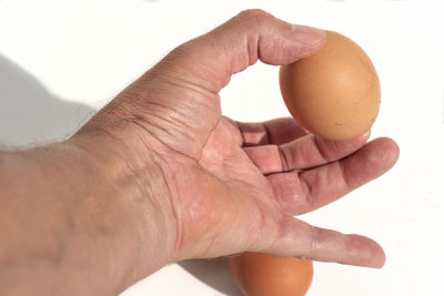 Cropped hand of person holding egg against white background