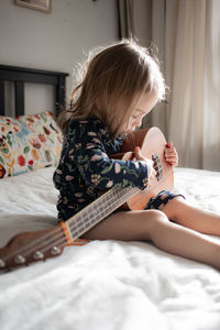 Boy playing guitar while lying on bed at home