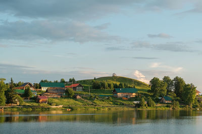 Houses by lake and buildings against sky