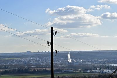 Electricity pylon by tree against sky